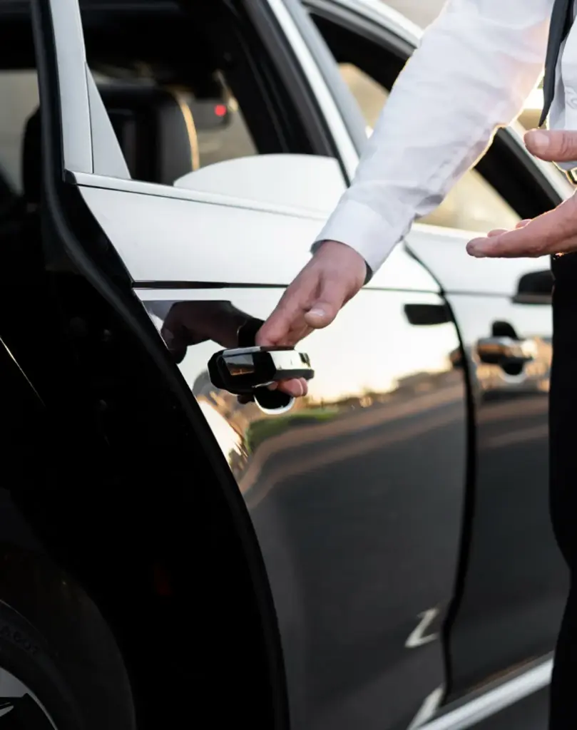 Een close-up van een hand die de achterdeur van een glanzend zwarte luxe auto opent, met een gedeeltelijk zichtbare gele knop in de rechterbovenhoek