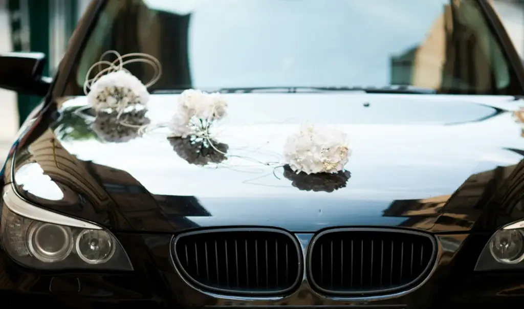 De voorkant van een zwarte BMW-trouwauto, elegant versierd met witte bloemstukken op de motorkap